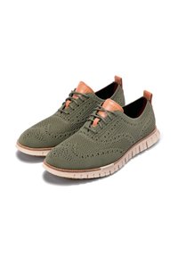 Olivově zelené pletené boty s texturovaným svrškem, koženými akcenty v barvě tan a flexibilní bílou podrážkou. Disponují šněrovacím designem a prodyšným materiálem.