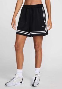 Black athletic shorts with white stripes, an elastic waistband, and a drawstring feature. Paired with white and black sneakers and socks.
