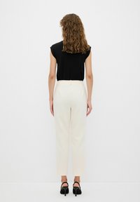Zwart, kort mouwtopje gecombineerd met crèmekleurige, op maat gemaakte broek. De broek heeft een naadloos ontwerp en wordt aangevuld met zwarte haksandalen.