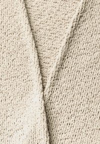 Texturiertes beige Stoff mit einer weichen, gewebten Optik, der ein V-Ausschnitt-Design und ein leicht geschlungenes Oberflächenmuster aufweist.