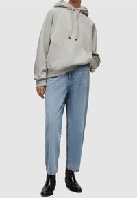 Felpa oversize grigia con tasca frontale, abbinata a jeans azzurri a gamba dritta e stivaletti neri alla caviglia, creando un look casual.