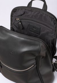Black leather backpack with a zippered front pocket, smooth texture, and interior pocket. Features a logo patch and fabric lining.