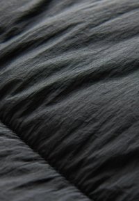 Tela negra arrugada con textura y ondulaciones visibles, posiblemente de nailon, que muestra un suave brillo y apariencia ligera.