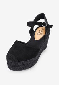Sandal de cuña espadrille negra con parte superior de ante y tira en el tobillo. Presenta suela de cuerda trenzada y puntera redondeada. Forro interior suave.