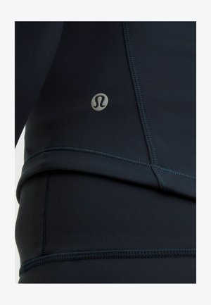 Czarna sportowa bluzka wykonana z elastycznego materiału. Posiada płaskie szwy i srebrny akcent z logo z boku. Gładka tekstura, dopasowany krój.