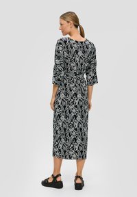 Zwart-wit paisleypatroon jurk met driekwart mouwen, een getailleerde taille en een rechte midi-lengte, gecombineerd met zwarte platformsandalen.
