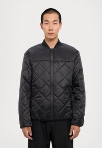 Fekete steppelt dzseki cipzáros elülső résszel, bordás gallérral és oldalsó zsebekkel. Simább, fényes anyagból készült, gyémántmintával.