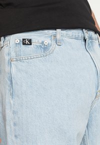Ljust blå jeans i denim har en framficka med silverdetaljer och en svart etikett med vitt "cK"-logotyp. Enkel design och klassisk passform.