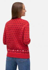 Suéter de punto rojo con lunares más oscuros y un patrón blanco en el dobladillo. Presenta un cuello y puños de canalé, corte estándar.