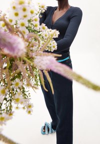 Námořnický žebrovaný top s dlouhým rukávem a tmavé džínové kalhoty, doplněné světle modrými spirálovými sandály, obklopené růžovými a bílými květinami.