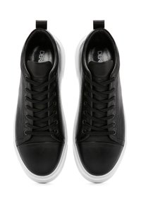 Sneaker in pelle nera con suola in gomma bianca, punta rotonda e lacci piatti. Presenta una texture liscia e una fascia sul tallone.