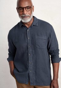 Camicia in lino di colore blu scuro con colletto, chiusura anteriore con bottoni e una tasca sul petto. Presenta maniche arrotolate e tessuto testurizzato.