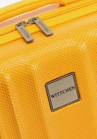 Žlutý tvrdý kufr s šestiúhelníkovým vzorem, vybavený stříbrnými zipy s vygravírovaným názvem značky "WITTCEN" a kovovou štítkovou destičkou.