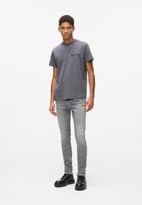 Pelēka kokvilnas T-krekli ar apaļu kaklu un melnu logotipu. Apvienots ar gaiši pelēkām šaurajām biksēm un melniem šņorējamiem zābakiem. Vienkāršs dizains.