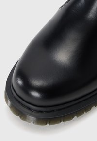 Zwarte leren laars met een glad, glanzend oppervlak, ronde neus, contrasterende gestructureerde rubberen zool en zichtbare stiksels langs de rand.