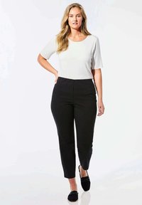 Haut blanc à manches courtes associé à un pantalon noir ajusté ; texture lisse, couleurs unies et design décontracté, porté avec des chaussures plates noires.