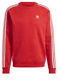 Felpa rossa con scollo tondo. Dettagli bianchi a tre strisce sulle maniche e piccolo logo Adidas bianco sul petto. Materiale in cotone.
