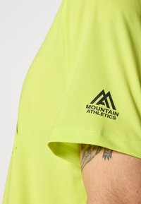 T-shirt de sport jaune fluo à manches courtes, avec un logo noir "Mountain Athletics" sur la manche, texture lisse et design ajusté.