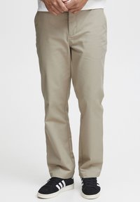 Beige cotton chinos with a straight-leg design, featuring front pockets, a zip fly, and worn with black athletic shoes.