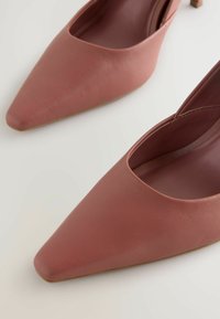 Scarpe slingback in pelle rosa con punta appuntita e tacco basso. Texture liscia e ampia apertura per il piede. Design semplice senza hardware visibile.