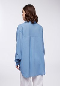 Camicia azzurro chiaro a maniche lunghe realizzata in un tessuto texturizzato, con colletto, cucitura a yoke sul retro e orlo curvo.
