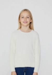 Weiße, flauschige Strickjacke mit rundem Ausschnitt und langen Ärmeln, kombiniert mit blauen Denim-Jeans, minimalistisches Design, weiche Textur.