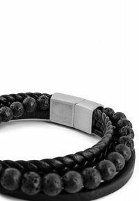 Black leather bracelet featuring braided texture, round lava stone beads, and a metallic clasp with engraved logo.