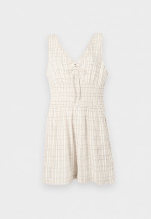 Ærmeløs beige kjole med diskret ternet mønster, V-hals, samlet talje og en lille dekorativ sløjfe i midten foran.