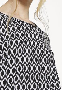 Top a pattern bianco e nero con un design geometrico, una texture morbida e uno scollo a barca.