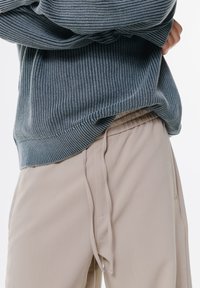 Pull en maille côtelée gris associé à un pantalon beige à taille élastique. Le pull présente un motif texturé, et le pantalon est doté de détails à cordon de serrage.