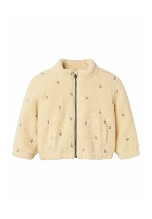 Veste en polaire crème avec fermeture éclair sur le devant, silhouette courte, deux poches latérales et broderies florales roses et noires sur l'ensemble.
