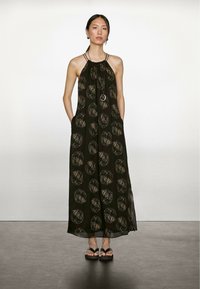 Maxi kjole i sort stof med store beige cirkulære mønstre, featuring en samlet halsudskæring og justerbare stropper. Indeholder sidelommer.