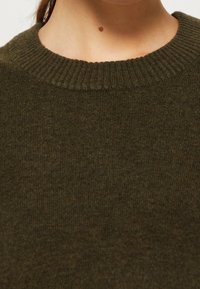 Olivgrön stickad tröja med ribbad rundhals och mjuk textur, med jämn sömnad och en subtil lyster.