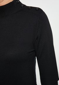 Schwarzes Strickoberteil mit hohem Ausschnitt, drei schwarzen Knöpfen an der Schulter und dreiviertellangen Ärmeln, mit einer glatten Textur.
