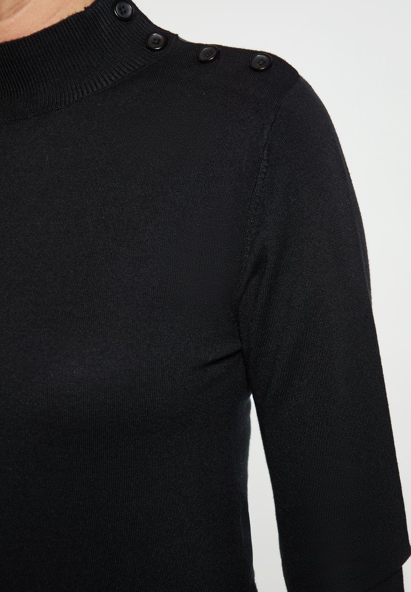 Schwarzes Strickoberteil mit hohem Ausschnitt, drei schwarzen Knöpfen an der Schulter und dreiviertellangen Ärmeln, mit einer glatten Textur.