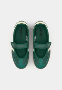 Grønne sportssko med borrelås, med en glatt overdel, teksturerte detaljer og en brun gummisåle. Adidas-logoen er trykt inni.
