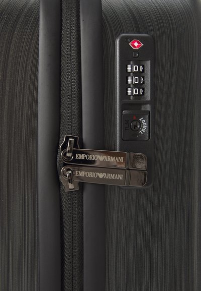 Căpăcel texturat de la o valiză neagră, cu două mânere împachetate Emporio Armani și un lacăt cu combinație aprobat de TSA, setat pe 000.