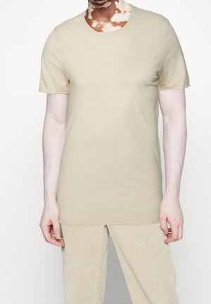 Beżowa bawełniana koszulka z krótkim rękawem, okrągłym dekoltem i gładką teksturą. Łączona z beżowymi spodniami sztruksowymi.