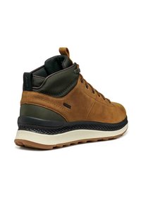 Botte de randonnée marron et vert foncé à lacets avec soutien de la cheville rembourré et semelle texturée noire et blanche, inclinée pour montrer le côté extérieur et le talon.