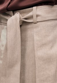 Pantalon en tissu beige à motif chevrons avec ceinture en tissu nouée et haut bordeaux rentré.
