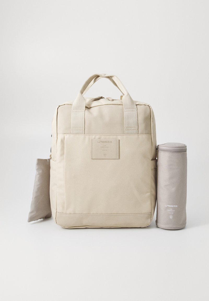 Sac à dos beige avec deux poignées supérieures, une poche avant et une pochette cylindrique assortie, fabriqué dans un tissu lisse et résistant.