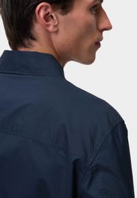 Mørkeblå skjorte med standard krave, der har en glat tekstur og rene linjer. Set fra ryggen, der viser skuldersøm-detaljer.