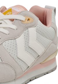 Sneaker grigia e bianca con dettagli perforati, design a zigzag a contrasto, accenti rosa e materiali in suede e pelle testurizzati.