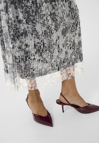 Bārkota kleita ar melnbaltu pērļu rakstu un caurspīdīgu apakšmali, kombinēta ar norādītām burgundijas slingback papēžiem.