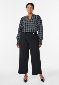 Melnas un baltas rūtainas blūzes ar pūkainām piedurknēm un v veida izgriezumu, kopā ar plašām melnām biksēm ar pogu detaļām un gludu tekstūru.