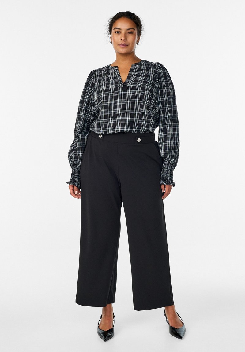 Melnas un baltas rūtainas blūzes ar pūkainām piedurknēm un v veida izgriezumu, kopā ar plašām melnām biksēm ar pogu detaļām un gludu tekstūru.