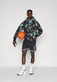 Sudadera negra con acentos turquesa y patrón abstracto, combinada con pantalones cortos de malla negros con detalles blancos, sosteniendo un balón de baloncesto naranja.