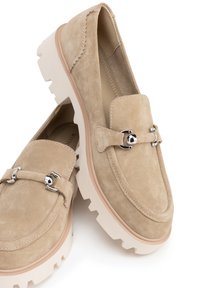 Los mocasines de ante beige cuentan con una gruesa suela de goma blanca, acentos de hardware en plata y detalles de costura alrededor de los bordes.