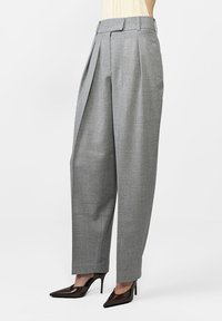 Szürke pliszírozott nadrág texturált anyagból, tapered lábbal és széles derékkal. Fényes, hegyes orrú, magassarkú cipőkkel párosítva.