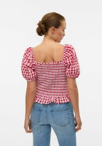 Top a maniche puff a quadretti rossi e bianchi con texture smock e design a schiena quadrata, abbinato a jeans in denim blu.